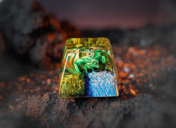 A hand-sculpted resin keycap featuring a miniature green dragon amid a waterfall scene — turns one key on your mechanical keyboard into a tiny diorama.
