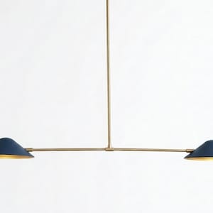 May include: A modern, minimalist pendant light fixture. It features a brass-colored frame with two navy blue, cone-shaped shades. The shades have a gold interior. The light hangs from a single vertical rod.