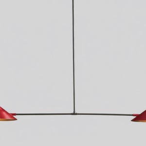 Puede incluir: Una lámpara colgante moderna y minimalista. Cuenta con dos pantallas rojas en forma de cono con interior dorado, suspendidas de una barra negra. La lámpara está diseñada para la iluminación cenital.