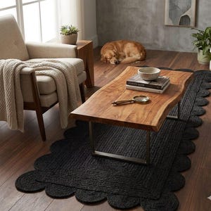 May include: A rectangular black jute rug featuring a scalloped edge design. The rug is woven with a thick, textured fiber construction and lies flat on a dark wooden floor, providing a solid foundation for the wooden coffee table placed above it.