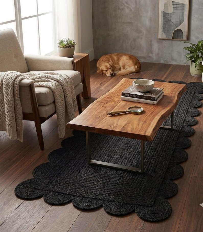 May include: A rectangular black jute rug featuring a scalloped edge design. The rug is woven with a thick, textured fiber construction and lies flat on a dark wooden floor, providing a solid foundation for the wooden coffee table placed above it.