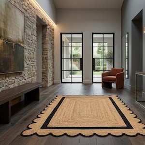 May include: A rectangular area rug featuring a natural tan woven fiber center, a thick black rectangular border, and a decorative scalloped edge finished with a black trim, placed on a dark wooden floor in a hallway setting.