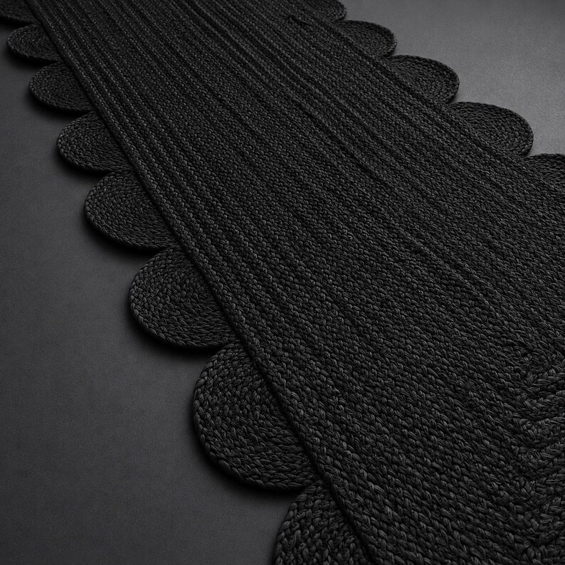 May include: A long, rectangular black table runner featuring a textured, braided construction. The edges of the runner are finished with a series of repeating, rounded scalloped shapes that extend along both sides of the central woven panel.