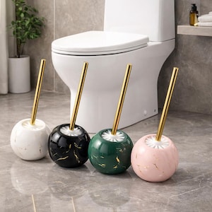 May include: Four decorative toilet bowl brushes with gold-colored handles and marble-patterned spheres in white, black, green, and pink. The brushes are displayed in front of a white toilet.