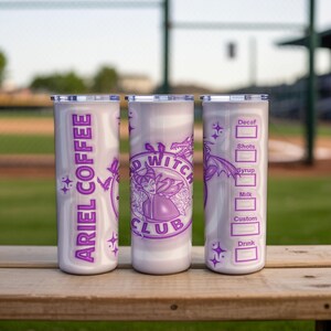 May include: Three white insulated tumblers with purple graphics and text. One tumbler reads "ARIEL COFFEE" vertically. The center tumbler features a witch design and the words "BAD WITCH CLUB". The third tumbler has a coffee order form.
