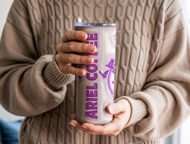 May include: A stainless steel tumbler with a purple design and the text "ARIEL COFFEE". The tumbler has a white straw and a silver lid. The design includes a clock and birds.