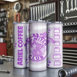 May include: Three silver insulated tumblers with purple graphics and text. One tumbler reads "ARIEL COFFEE" vertically. Another features a purple witch design and "BAD WITCH CLUB". The third has a coffee order form. The tumblers are on a metal surface.
