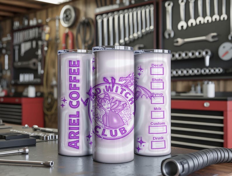 May include: Three silver insulated tumblers with purple graphics and text. One tumbler reads "ARIEL COFFEE" vertically. Another features a purple witch design and "BAD WITCH CLUB". The third has a coffee order form. The tumblers are on a metal surface.