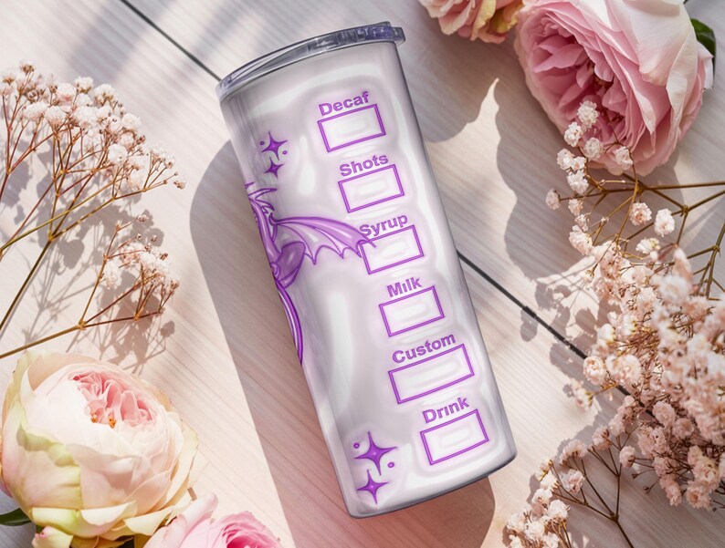 May include: A white tumbler with a purple dragon design and text boxes for drink customization. The tumbler includes labels for Decaf, Shots, Syrup, Milk, Custom, and Drink. The background features pink roses and white flowers.