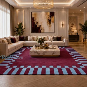 Peut inclure: Un grand tapis rectangulaire doté d'un centre bordeaux profond et d'une large bordure composée de blocs rectangulaires alternant bleu clair et bordeaux. Le tapis est placé sur un parquet clair dans un salon avec un canapé et une table blancs.