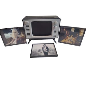 May include: A black and white retro-style television with a black screen, white accents, and four small legs. The television is surrounded by four framed images featuring scenes from a horror movie. The images are black and white and color.