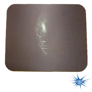 May include: A dark gray mouse pad with a white outline of an alien's head.