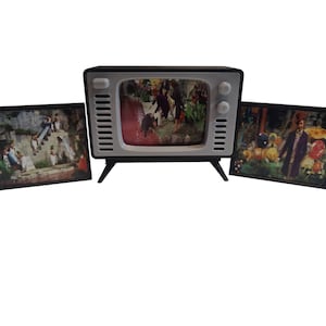 Puede incluir: Un televisor de estilo retro con un marco en blanco y negro, que muestra una escena colorida. Dos imágenes enmarcadas flanquean el televisor, cada una mostrando una escena diferente. El televisor tiene una pantalla blanca y patas negras.