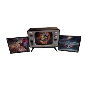 May include: A retro-style black and white television with a screen displaying a scene from Star Trek. Two framed images flank the TV, one with a group of people and the other with a spaceship.