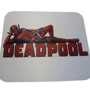 May include: A white mousepad with a red and black Deadpool character lying on top of the word "DEADPOOL" in red letters.