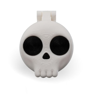 May include: A white plastic skull-shaped container with black eyes. The container has a hinged lid.
