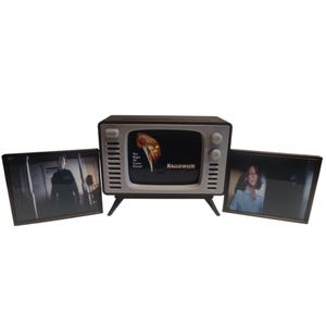 Könnte beinhalten: Ein Fernseher im Retro-Stil mit einem schwarzen Bildschirm, auf dem ein Halloween-Filmplakat zu sehen ist. Zwei gerahmte Bilder flankieren den Fernseher und zeigen Szenen aus dem Film. Der Fernseher ist schwarz und silber, ideal für Horrorfilm-Fans.