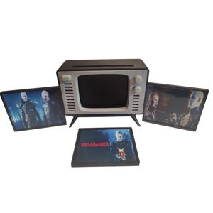 May include: A black and white retro-style television set with three framed images. The images feature characters from the horror film "Hellraiser". The TV has a black screen and white accents. The framed images are rectangular and feature various scenes from the movie.