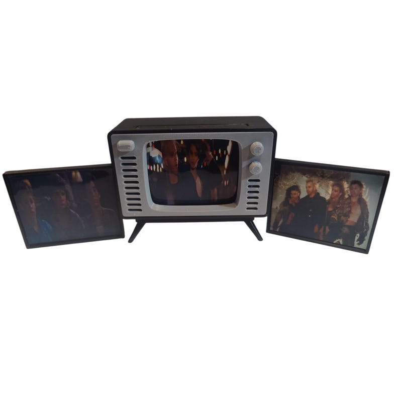 May include: A miniature black and white television with a screen displaying a movie scene. Two additional framed images flank the TV, also showing movie stills. The TV has a retro design with knobs and a small screen.