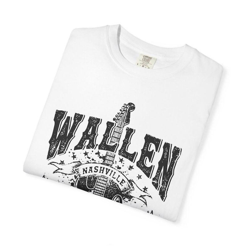May include: White t-shirt with a black graphic design. The design features the name "WALLEN" in a distressed font, a guitar, and the word "NASHVILLE" on a banner. The shirt is folded.