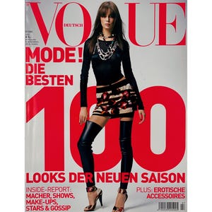 May include: Vogue Deutsch magazine cover featuring a model in a black top, patterned mini-skirt, and thigh-high black boots. The cover has large red text that reads "Vogue Deutsch", "Mode! Die Besten", and "100". Additional text includes "Looks der neuen Saison".