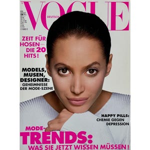 May include: Vogue Deutsch magazine cover with a woman in a white top. The cover features the Vogue logo in pink and white, and text in German. Headlines include "Zeit für Hosen - Die 20 Hits!" and "Happy Pills: Chemie gegen Depression."