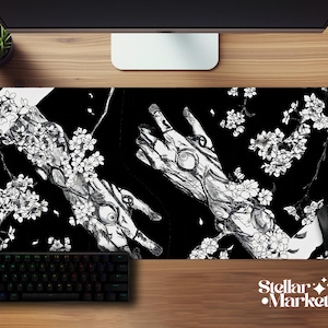 May include: Black and white desk mat with a detailed illustration of hands and cherry blossom branches. Includes a keyboard, mouse, and the Stellar Market logo.