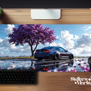 May include: A rectangular mousepad featuring a dark blue sports car parked near a vibrant purple flowering tree. The background shows a blue sky with fluffy white clouds. A black keyboard and mouse are visible.