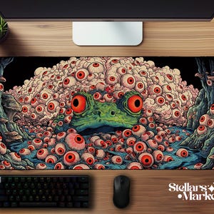 May include: A rectangular desk mat featuring a surreal illustration of a large green frog surrounded by a dense cluster of numerous human-like eyeballs with red irises. The scene includes dark blue water, rocky formations, and mushrooms.