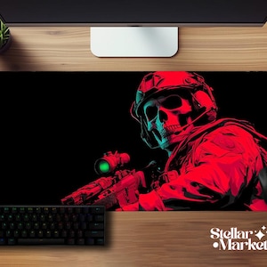 Puede incluir: Alfombrilla de ratón para juegos negra con una ilustración roja y verde azulado de una calavera con casco militar apuntando con un rifle. También se ven un teclado y un ratón negros. El logotipo de Stellar Market está en la esquina inferior derecha.
