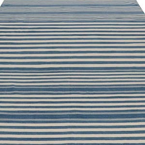 May include: A large, rectangular rug with a striped pattern. The rug features alternating horizontal stripes of blue and off-white, creating a simple yet visually appealing design. The rug is made of a woven material.