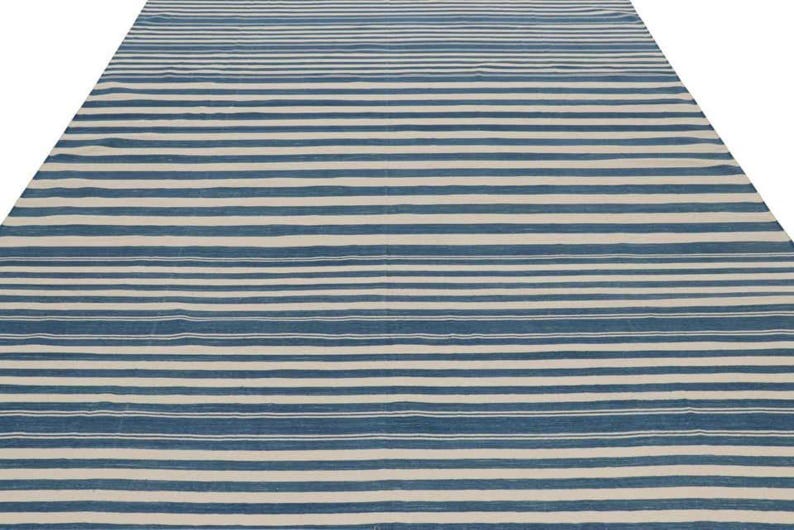 May include: A large, rectangular rug with a striped pattern. The rug features alternating horizontal stripes of blue and off-white, creating a simple yet visually appealing design. The rug is made of a woven material.