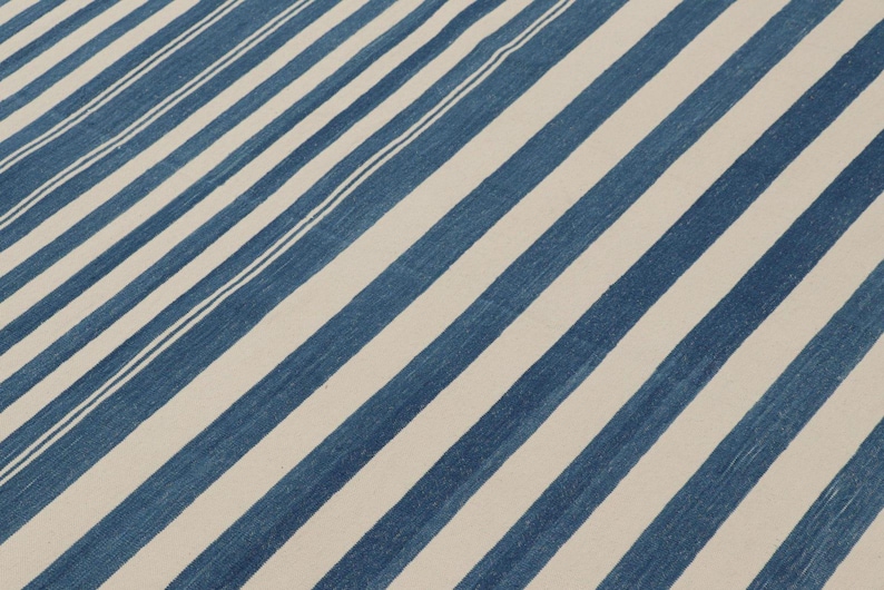 May include: A rug with a repeating pattern of wide, diagonal stripes in navy blue and off-white. The stripes are evenly spaced, creating a bold, graphic design. The rug appears to be made of a woven material.