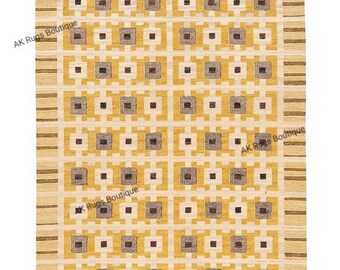 May include: A rectangular rug with a geometric pattern in shades of yellow, brown, and cream. The design features repeating squares and rectangles, with the text "AK Rugs Boutique" along the edges. The rug has a textured appearance.