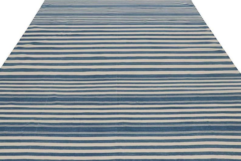 May include: A large, rectangular rug with a striped pattern. The rug features alternating horizontal stripes of blue and off-white. The stripes are evenly spaced, creating a simple yet visually appealing design. The rug is likely made of a woven material.