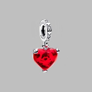 Puede incluir: Un charm de plata con un colgante en forma de coraz&oacute;n rojo. El coraz&oacute;n tiene una apariencia texturizada y est&aacute; suspendido de un anillo de plata con la palabra "Pandora" y el logotipo de Disney. El anillo est&aacute; adornado con peque&ntilde;as piedras transparentes.