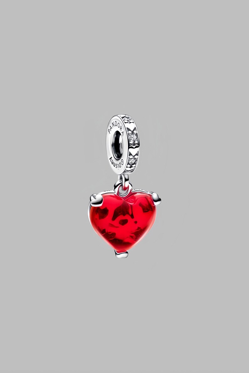 Puede incluir: Un charm de plata con un colgante en forma de coraz&oacute;n rojo. El coraz&oacute;n tiene una apariencia texturizada y est&aacute; suspendido de un anillo de plata con la palabra "Pandora" y el logotipo de Disney. El anillo est&aacute; adornado con peque&ntilde;as piedras transparentes.