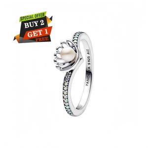 May include: A sterling silver ring featuring a central white pearl set within a shell-shaped motif. The band is accented with a row of small, clear, sparkling stones and is engraved with the text PANDORA S925 ALE on the inner surface.