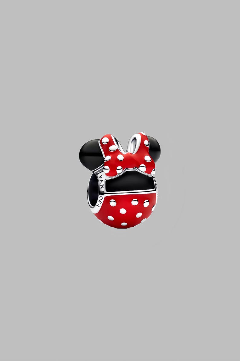 Puede incluir: Un charm rojo con lunares blancos, orejas negras y un lazo a juego. El charm es una representaci&oacute;n estilizada de un famoso personaje de dibujos animados. La palabra "PANDORA" est&aacute; grabada en el lateral.