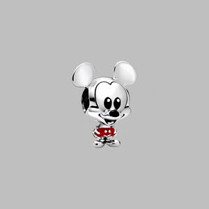 Peut inclure: Un charm en argent repr&eacute;sentant Mickey Mouse. Le charm pr&eacute;sente les grandes oreilles de Mickey, son visage souriant et un short rouge &agrave; pois blancs. Le charm est tr&egrave;s d&eacute;taill&eacute; et a une finition polie, sur fond gris.