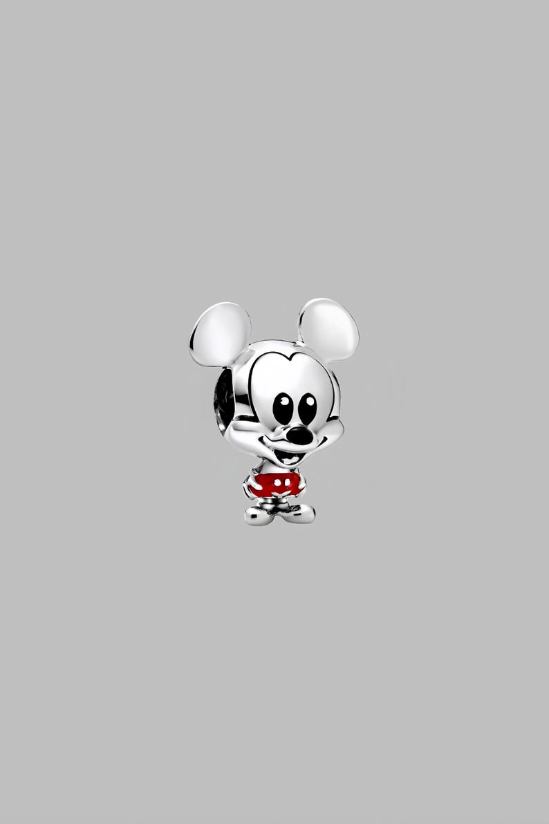 Peut inclure: Un charm en argent repr&eacute;sentant Mickey Mouse. Le charm pr&eacute;sente les grandes oreilles de Mickey, son visage souriant et un short rouge &agrave; pois blancs. Le charm est tr&egrave;s d&eacute;taill&eacute; et a une finition polie, sur fond gris.