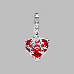Puede incluir: Un charm de plata con un colgante rojo en forma de coraz&oacute;n. El colgante presenta un dise&ntilde;o de dos personajes de dibujos animados y un coraz&oacute;n. El charm tiene una banda decorativa con piedras transparentes en la parte superior.
