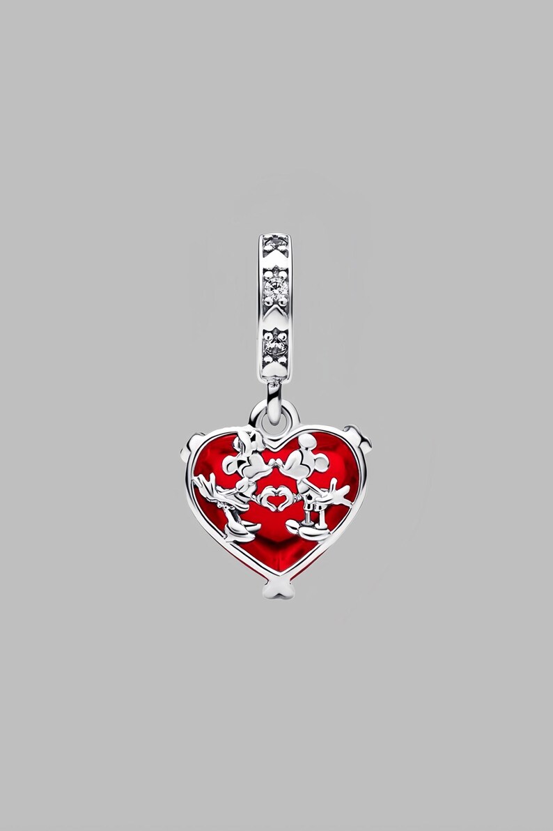 Puede incluir: Un charm de plata con un colgante rojo en forma de coraz&oacute;n. El colgante presenta un dise&ntilde;o de dos personajes de dibujos animados y un coraz&oacute;n. El charm tiene una banda decorativa con piedras transparentes en la parte superior.