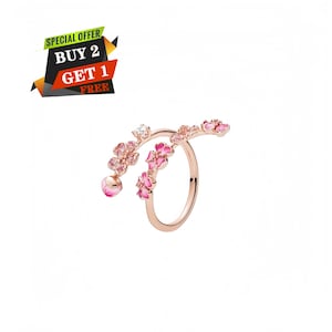 May include: Rose gold ring with pink flower and crystal accents. The ring features a floral design with multiple pink flowers and a dangling pink gem. The ring also has a small crystal. The image includes text that says "SPECIAL OFFER BUY 2 GET 1 FREE".