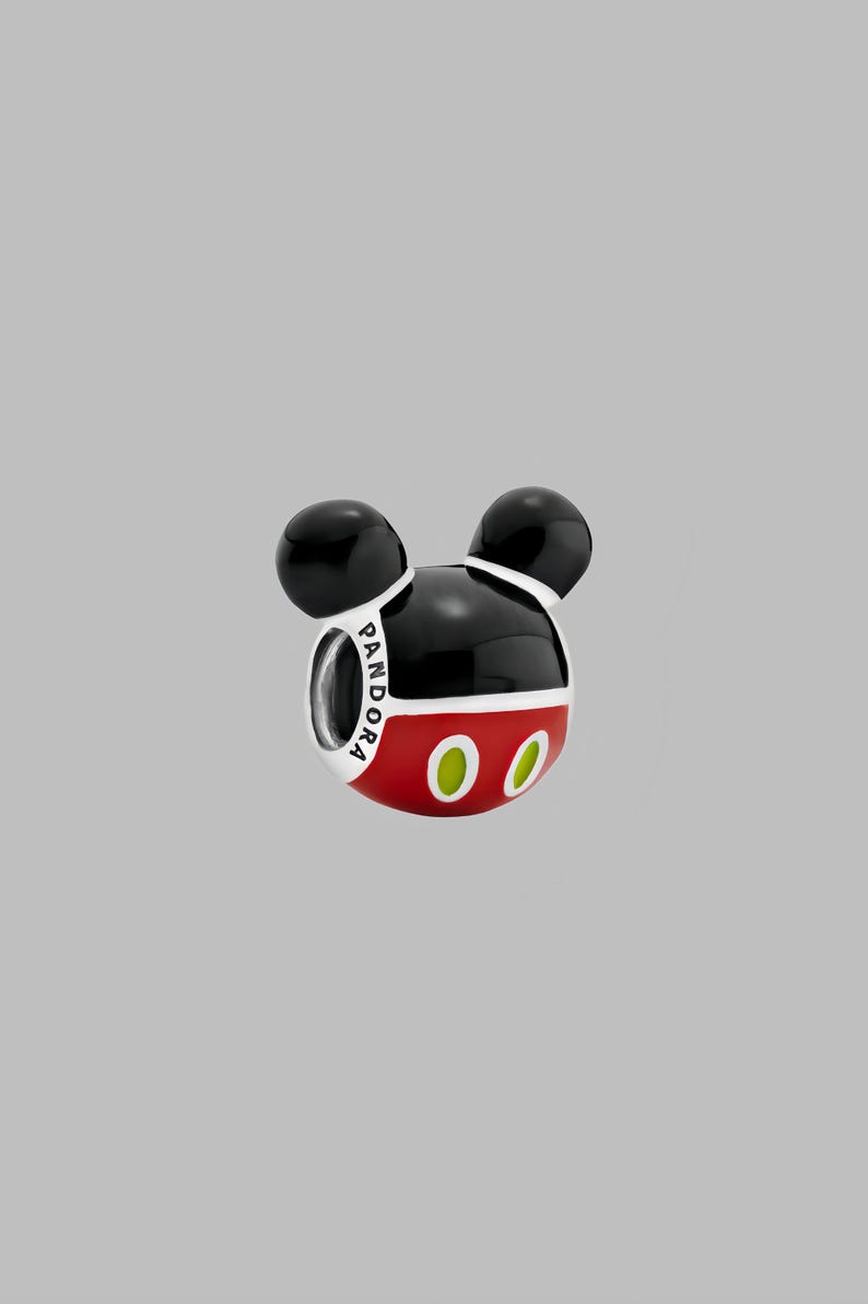 May include: A charm in the shape of Mickey Mouse's head. The charm is black and red with two black spheres for ears. The charm has the word "PANDORA" printed on it and two green ovals for eyes.