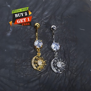 May include: Two belly button rings, one gold-toned and one silver-toned, each featuring a round clear stone at the top and a dangling charm shaped like a crescent moon and sun with small embedded stones. The text reads SPECIAL OFFER BUY 2 GET 1 FREE.
