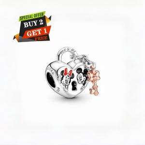 May include: A silver heart-shaped charm with Mickey and Minnie Mouse illustrations. The charm has a key and chain attached. The text "YOU & ME" is engraved on the top. The charm is a Disney-themed jewelry item.