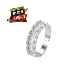 Puede incluir: Un anillo abierto de tono plateado con una fila central de piedras claras de corte baguette, flanqueada por dos filas de pequeñas perlas blancas y diminutas piedras claras redondas. Incluye el texto SPECIAL OFFER BUY 2 GET 1 FREE en la esquina.