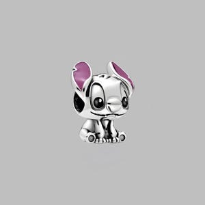 May include: A silver-colored charm depicting the character Stitch from the animated film Lilo & Stitch. The charm features Stitch's signature large ears with purple accents, big black eyes, and a small smile. The charm is a collectible item.