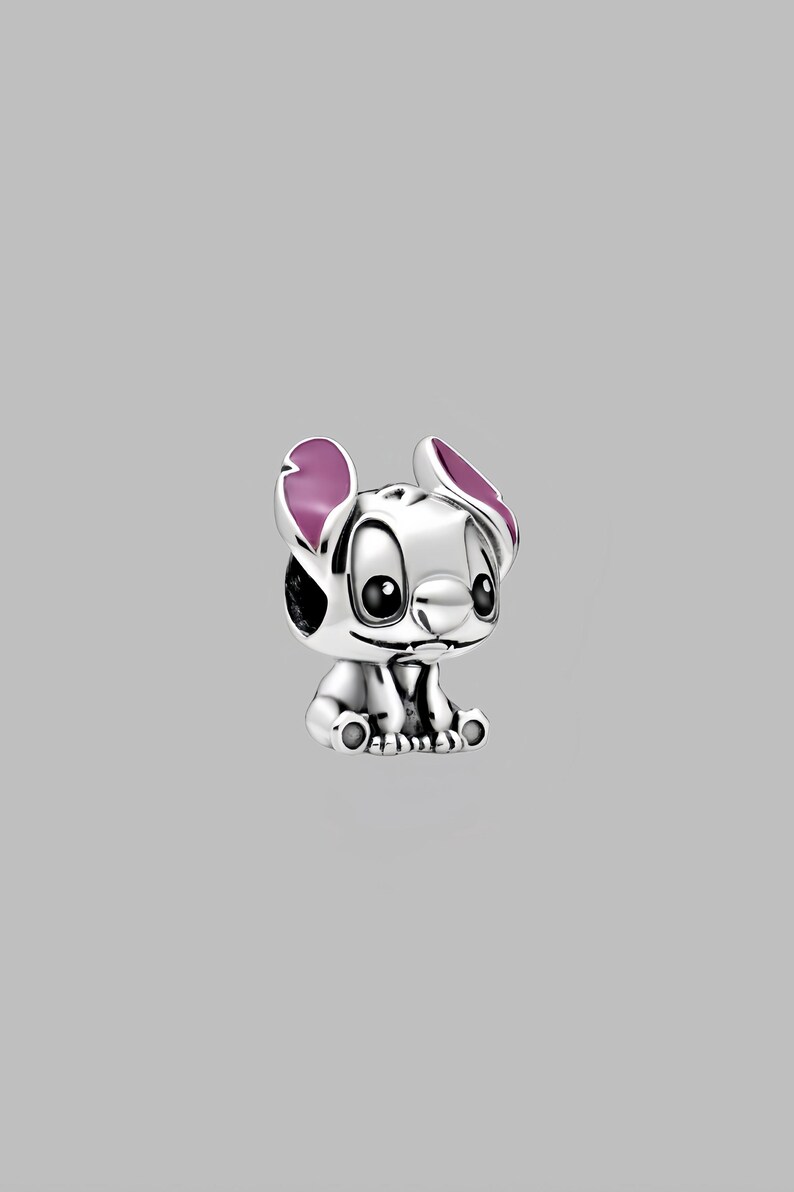 May include: A silver-colored charm depicting the character Stitch from the animated film Lilo & Stitch. The charm features Stitch's signature large ears with purple accents, big black eyes, and a small smile. The charm is a collectible item.